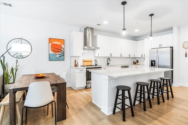 kitchen featuring wall chimney exhaust hood, white cabinetry, stainless steel appliances, and hanging light fixtures