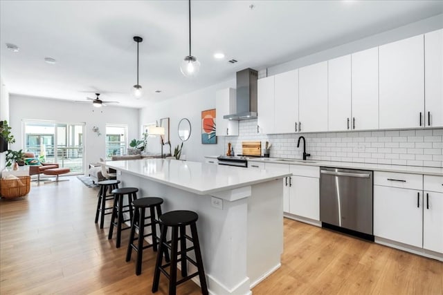 kitchen featuring stainless steel appliances, ceiling fan, wall chimney range hood, decorative light fixtures, and white cabinetry