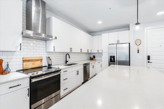 kitchen with sink, hanging light fixtures, wall chimney range hood, white cabinets, and appliances with stainless steel finishes