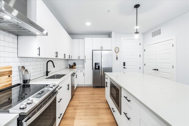 kitchen with wall chimney exhaust hood, stainless steel appliances, sink, pendant lighting, and white cabinetry