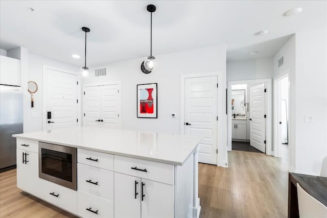 kitchen featuring pendant lighting, built in appliances, light hardwood / wood-style flooring, white cabinets, and a kitchen island