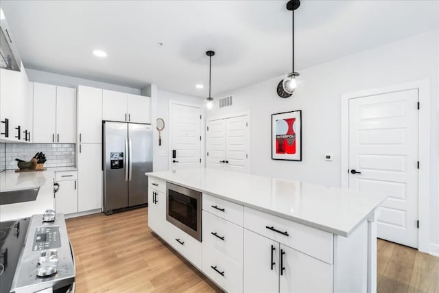 kitchen featuring built in microwave, a center island, stainless steel refrigerator with ice dispenser, decorative light fixtures, and white cabinets