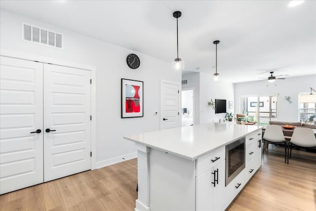 kitchen featuring white cabinetry, built in microwave, ceiling fan, light hardwood / wood-style floors, and decorative light fixtures