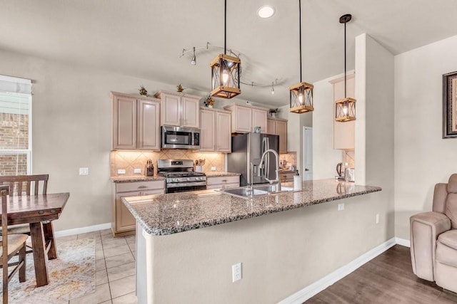 kitchen with sink, dark stone countertops, decorative light fixtures, kitchen peninsula, and stainless steel appliances