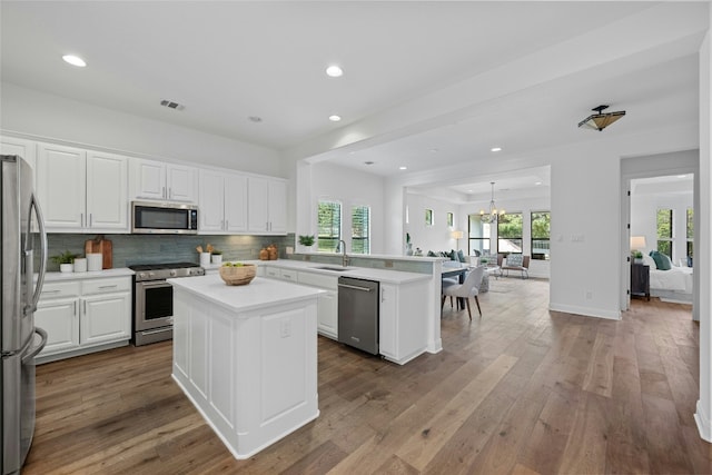 kitchen with sink, a kitchen island, kitchen peninsula, white cabinets, and appliances with stainless steel finishes