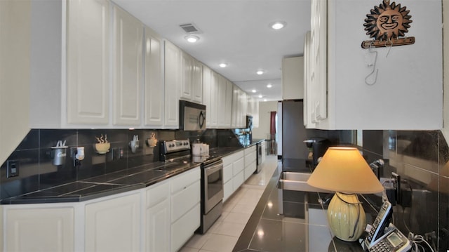 kitchen with stainless steel electric range, sink, tasteful backsplash, light tile patterned flooring, and white cabinetry