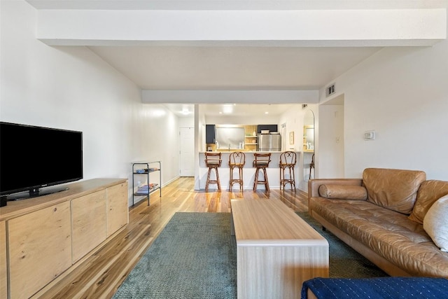 living room featuring light wood-style floors, visible vents, and beamed ceiling