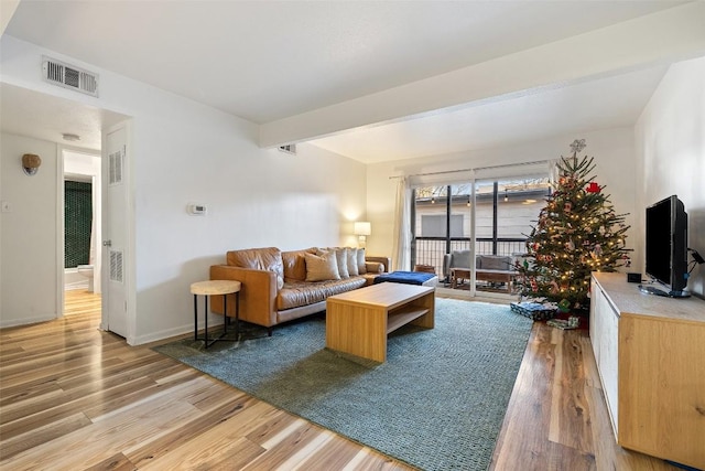 living room featuring light wood-type flooring, baseboards, visible vents, and beamed ceiling