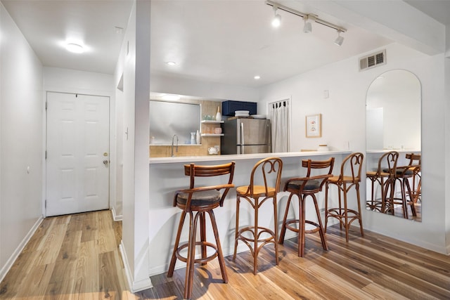 kitchen featuring blue cabinets, a breakfast bar, wood finished floors, visible vents, and freestanding refrigerator