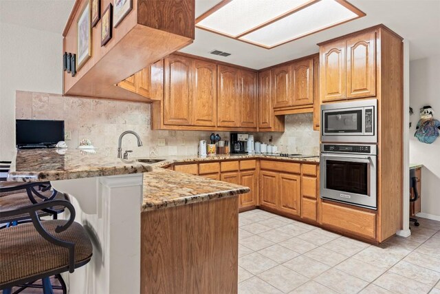 kitchen with light stone countertops, sink, stainless steel appliances, kitchen peninsula, and light tile patterned floors