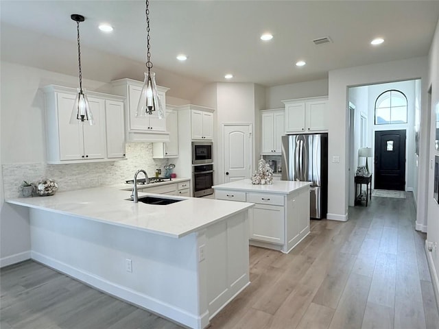 kitchen with kitchen peninsula, appliances with stainless steel finishes, decorative backsplash, decorative light fixtures, and a kitchen island