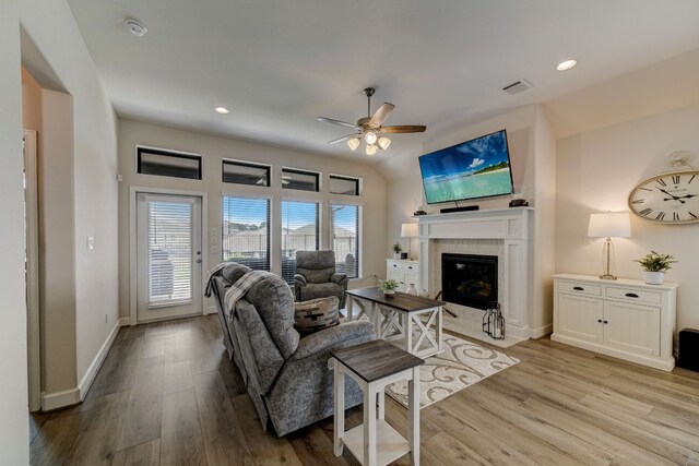 living room featuring wood finished floors, visible vents, baseboards, a ceiling fan, and a tiled fireplace