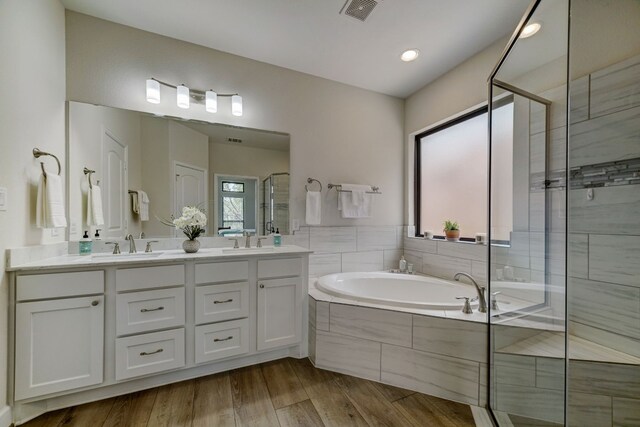 bathroom featuring visible vents, a shower stall, a garden tub, wood finished floors, and a sink