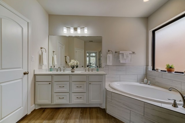 bathroom with a garden tub, wood finished floors, double vanity, and a sink