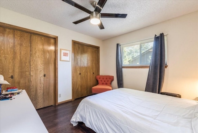 bedroom with a textured ceiling, ceiling fan, dark wood-type flooring, and two closets