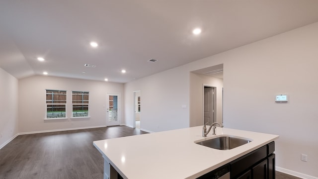 kitchen with a center island with sink, vaulted ceiling, sink, and dark wood-type flooring