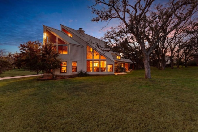 back house at dusk featuring a lawn