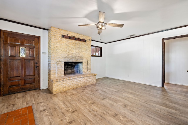 unfurnished living room featuring ceiling fan, wood-type flooring, crown molding, and a brick fireplace