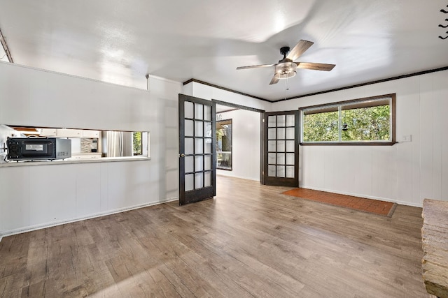 unfurnished living room with crown molding, french doors, ceiling fan, and light wood-type flooring