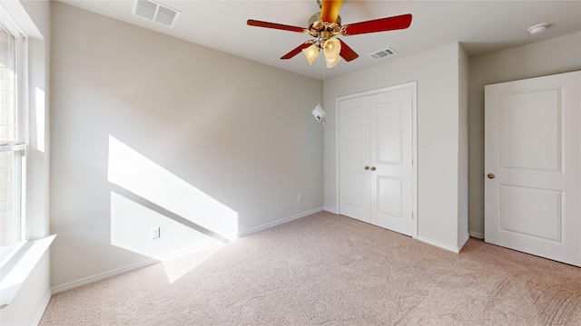 unfurnished bedroom with multiple windows, a closet, light colored carpet, and ceiling fan