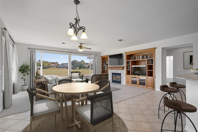 carpeted dining space with a tile fireplace and ceiling fan with notable chandelier