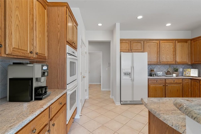 kitchen featuring decorative backsplash, light stone countertops, white appliances, and light tile patterned floors