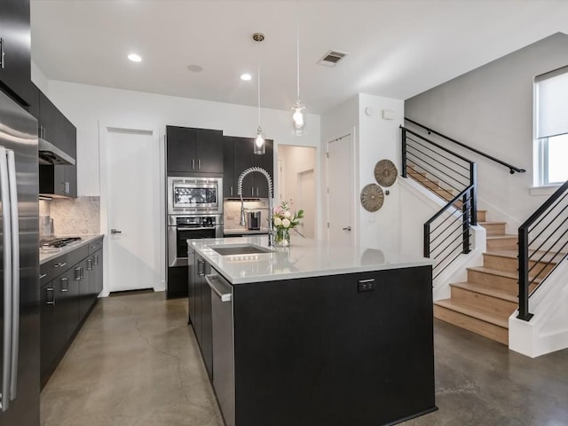 kitchen with sink, stainless steel appliances, hanging light fixtures, backsplash, and an island with sink