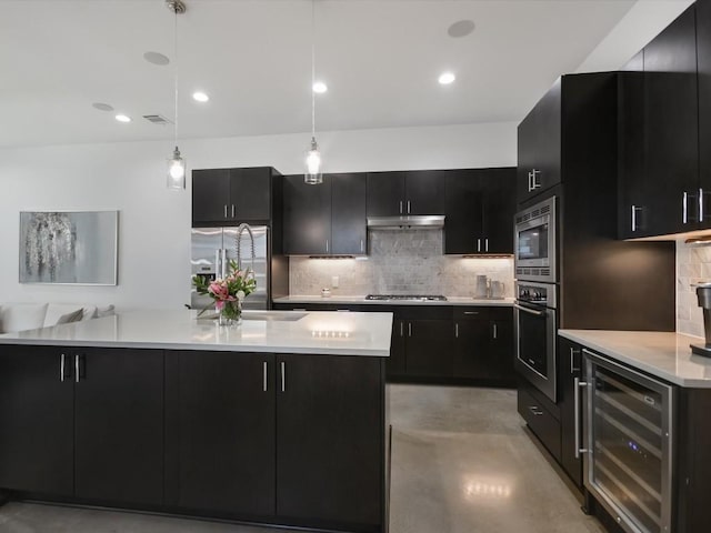 kitchen with wine cooler, backsplash, pendant lighting, a kitchen island with sink, and appliances with stainless steel finishes