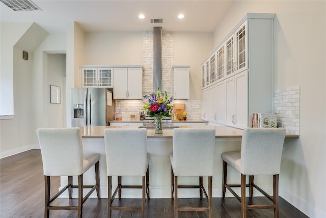 kitchen with white cabinetry, tasteful backsplash, stainless steel refrigerator with ice dispenser, kitchen peninsula, and a breakfast bar area