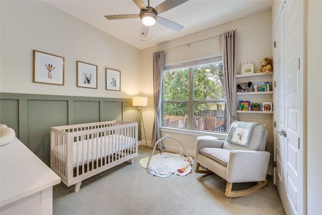 carpeted bedroom featuring a crib and ceiling fan