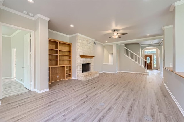 unfurnished living room with ceiling fan, built in shelves, ornamental molding, a fireplace, and light hardwood / wood-style floors