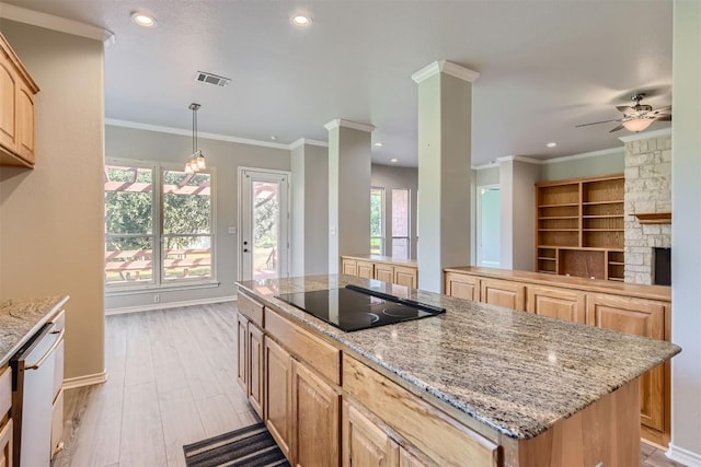 kitchen with black electric cooktop, ceiling fan, a kitchen island, hanging light fixtures, and a stone fireplace