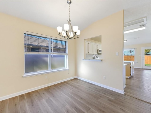 unfurnished dining area featuring a chandelier, vaulted ceiling, and light wood-type flooring