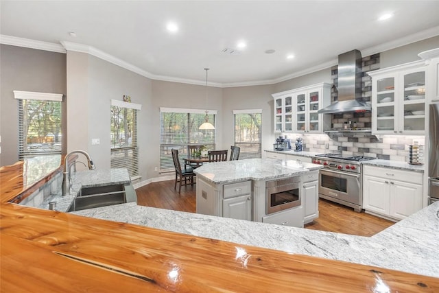 kitchen featuring appliances with stainless steel finishes, wall chimney exhaust hood, sink, white cabinets, and hanging light fixtures