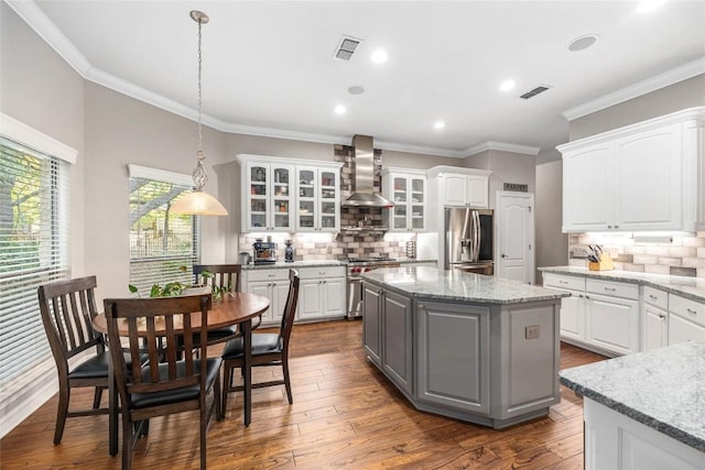 kitchen featuring wall chimney exhaust hood, hanging light fixtures, white cabinets, and stainless steel appliances