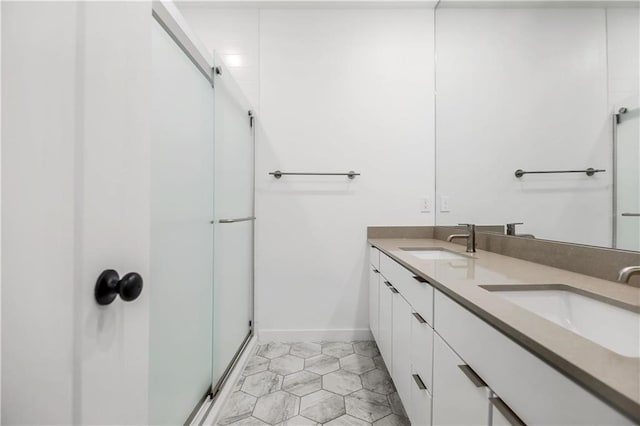 full bathroom with double vanity, a stall shower, baseboards, and a sink