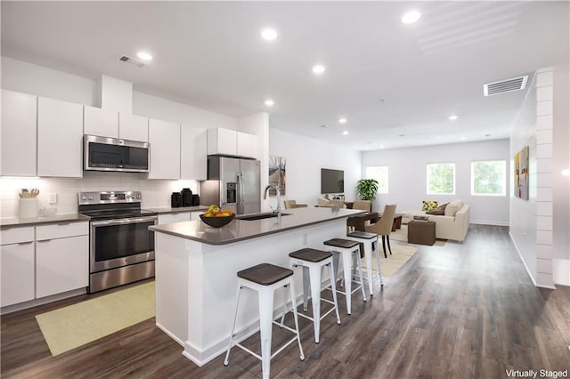 kitchen featuring appliances with stainless steel finishes, white cabinets, visible vents, and an island with sink