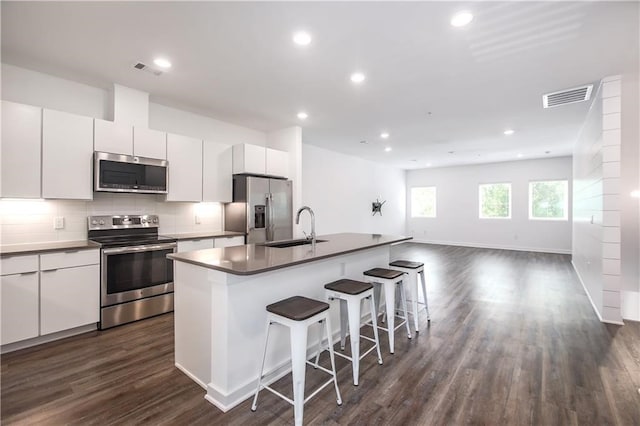 kitchen with stainless steel appliances, visible vents, a kitchen island with sink, a sink, and white cabinetry