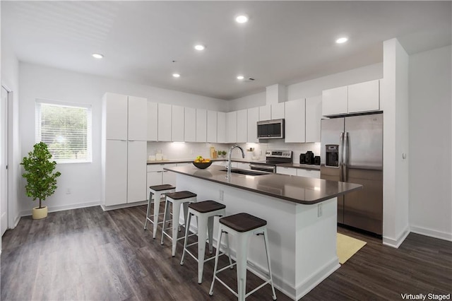 kitchen with a center island with sink, a breakfast bar area, dark countertops, appliances with stainless steel finishes, and white cabinets