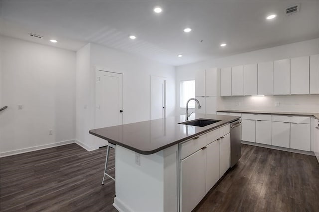 kitchen with sink, dark wood-type flooring, white cabinetry, a center island with sink, and stainless steel dishwasher