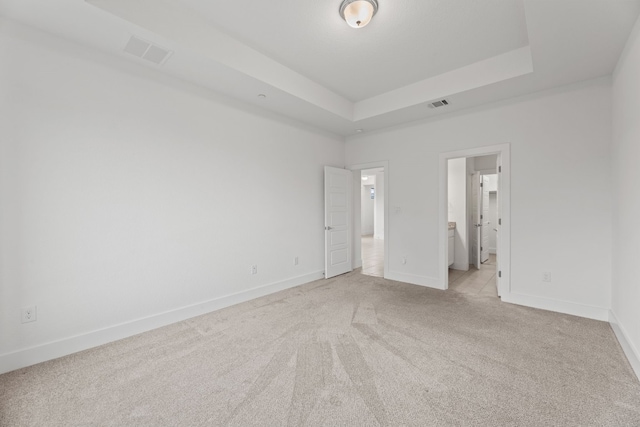 unfurnished bedroom featuring light carpet, ensuite bathroom, and a tray ceiling