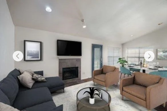 living room with a tiled fireplace and vaulted ceiling