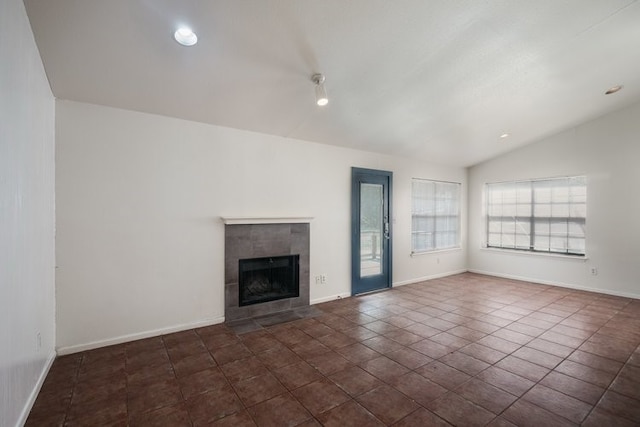 unfurnished living room with dark tile patterned flooring, lofted ceiling, and a tiled fireplace