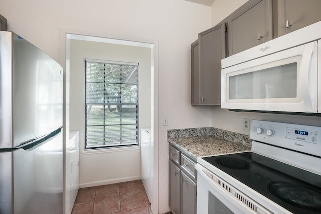 kitchen with gray cabinets, a wealth of natural light, light stone countertops, and white appliances