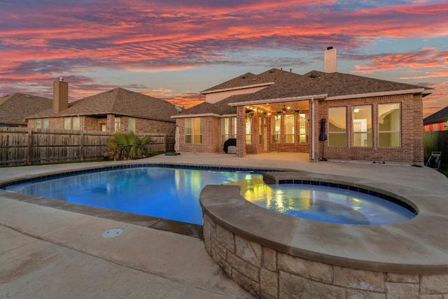 pool at dusk featuring an in ground hot tub and a patio