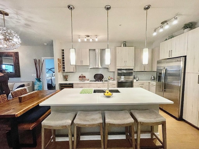 kitchen with a kitchen breakfast bar, hanging light fixtures, sink, wall chimney exhaust hood, and appliances with stainless steel finishes