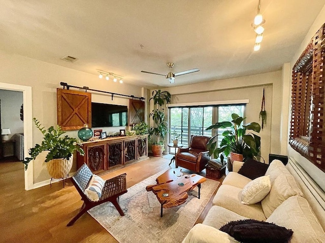 living room with ceiling fan, a barn door, and wood-type flooring