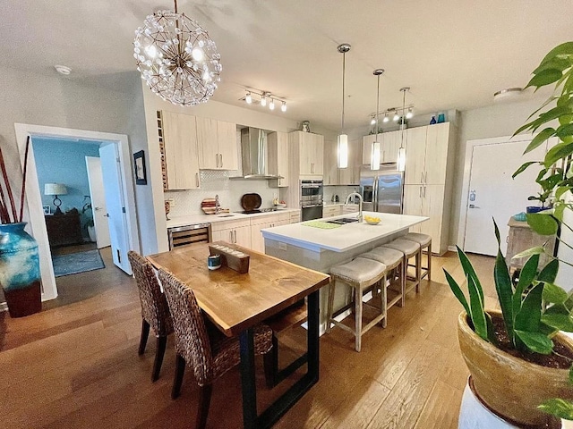 kitchen featuring stainless steel appliances, light hardwood / wood-style flooring, hanging light fixtures, and wall chimney exhaust hood