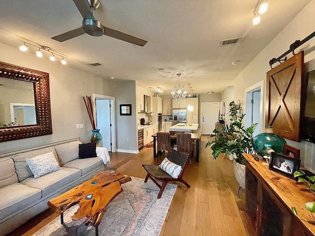 living room with ceiling fan with notable chandelier, a barn door, and light hardwood / wood-style flooring