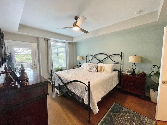 bedroom with a raised ceiling, ceiling fan, dark hardwood / wood-style flooring, and access to exterior